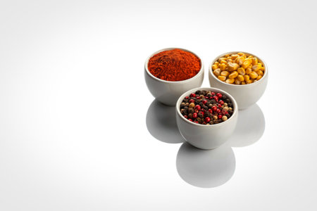 Three white ceramic bowls filled with colorful spices and grains are arranged on a reflective white surface, casting soft shadows.の写真素材