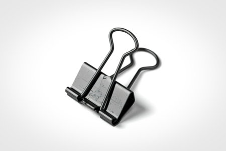 A close-up studio shot of two black metal binder clips resting on a clean white surface, casting a subtle shadow.の写真素材