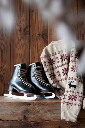 A pair of black ice skates rests beside a warm, patterned knit sweater, evoking a cozy winter atmosphere.の写真素材