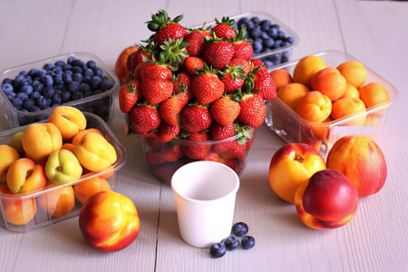 A vibrant assortment of fresh strawberries, blueberries, apricots, and nectarines are artfully displayed with a small white cup in the center.の写真素材