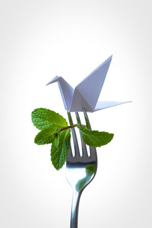A delicate origami crane rests atop a fork, adorned with vibrant green mint leaves, symbolizing nature and artistry.の写真素材