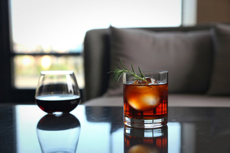 Two glasses of beverages sit on a reflective surface. One contains ice and a dark liquid, the other a dark red liquid.の写真素材