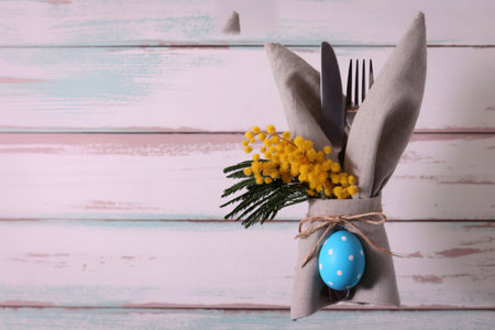 A festive Easter table setting featuring a napkin folded into a bunny shape, adorned with yellow flowers and a blue egg.の写真素材