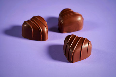 Three heart-shaped milk chocolate candies with decorative swirls are artfully arranged on a soft...
