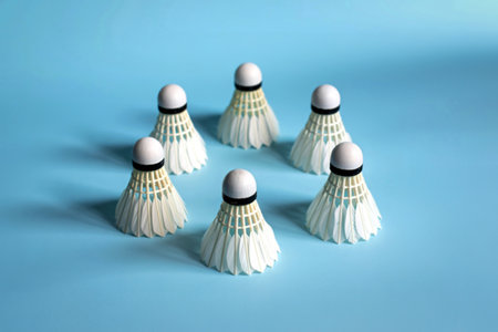 A group of six white badminton shuttlecocks are neatly arranged in a circular pattern on a smooth,...