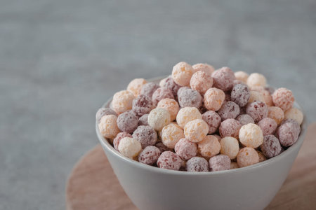 A white bowl filled with colorful cereal balls on a wooden boardの写真素材