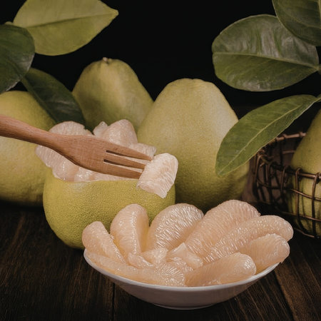 A bowl of peeled fruits with a fork, surrounded by whole fruits and green leaves on a wooden table.の写真素材