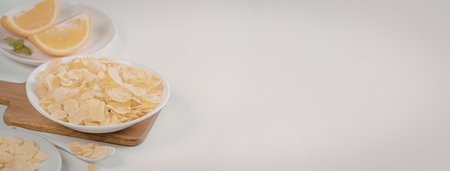 A bowl of cornflakes on a wooden cutting board with a plate of orange slices in the backgroundの写真素材