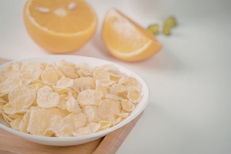 A bowl of corn flakes on a wooden board with orange slices in the background