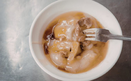 A white bowl containing dumplings in a savory broth with a forkの写真素材