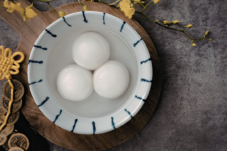A white bowl with blue lines contains three white balls, placed on a wooden plate with a yellow...