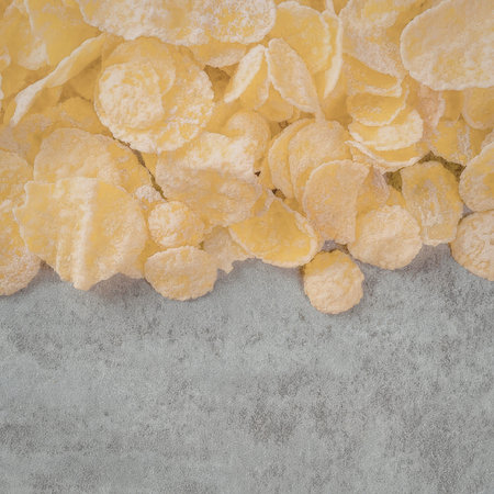 A close-up image of a pile of corn flakes on a gray surface, showcasing the cereal's texture and...