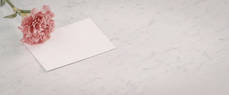 A pink flower is placed beside a white card on a marble surface.