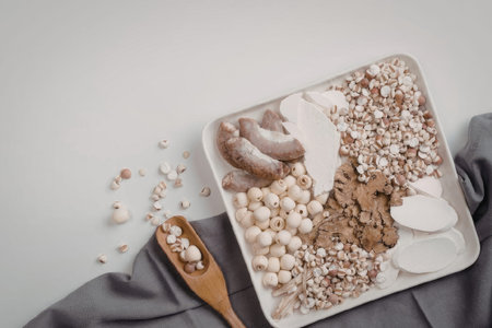A white plate filled with an assortment of grains, seeds, and other food items, accompanied by a wooden spoon on a gray cloth.の写真素材