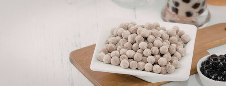 A white plate filled with tapioca pearls sits on a wooden cutting board, accompanied by a small bowl of black tapioca pearls and a glass with a brown and black drinkの写真素材