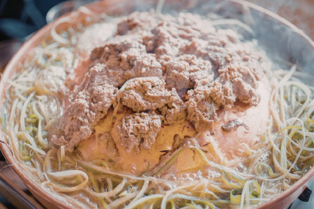 A close-up shot of a steaming hot dish of noodles and meat in a copper-colored bowl.