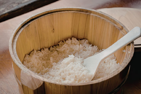 A wooden bucket filled with steamed rice and a white plastic spoon resting on top.