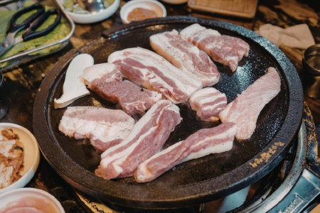 A close-up view of bacon strips sizzling on a hot plate, surrounded by various side dishesの写真素材