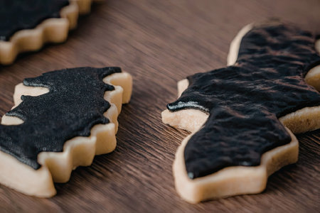 A close-up of bat shaped cookies with black icing on a wooden surface.