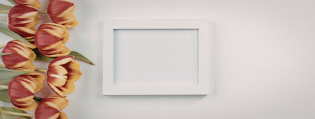 A bouquet of vibrant red and yellow tulips placed beside a blank white picture frame on a clean white background.の写真素材