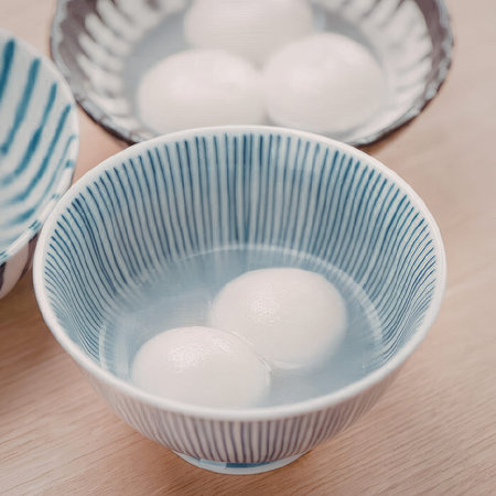 A blue and white bowl containing water and two white balls, with another bowl in the background.