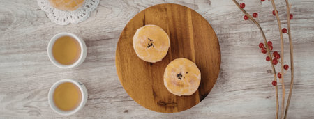 A wooden table with two cups of tea, two muffins on a wooden plate, and a branch with red berries.