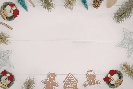 christmas decorations including gingerbread men, wreaths, and pine branches on white wooden backgroundの写真素材