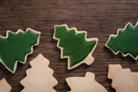 A close-up of Christmas tree shaped cookies, some iced green and others plain, on a wooden surface.