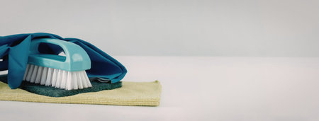 A blue cleaning brush with white bristles and a green cloth on a white surface