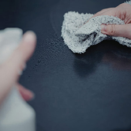 A person cleaning a dark surface with a white cloth and a bottle of cleaner