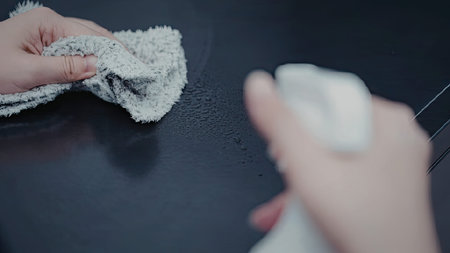 A person cleaning a dark surface with a white cloth and a spray bottle.