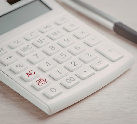 A white calculator with a pen on a wooden desk, emphasizing the calculator's keypad and display