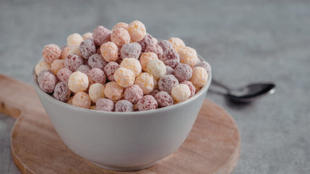 A white bowl filled with colorful cereal balls on a wooden board