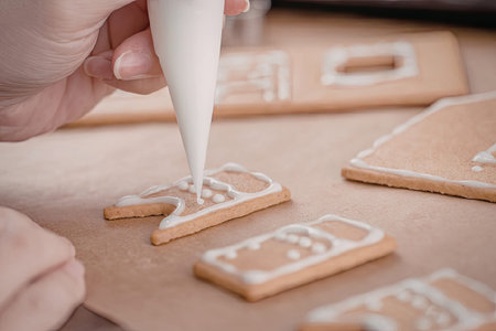 A hand decorating gingerbread pieces with white icing on a brown surface