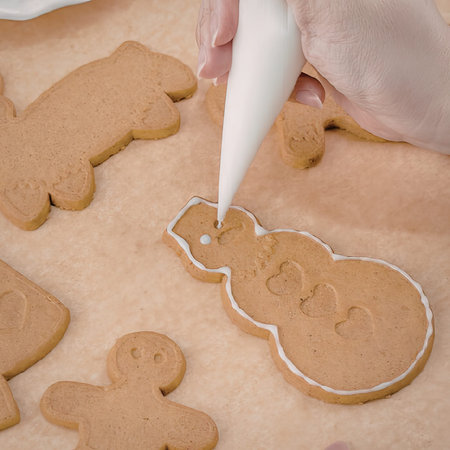 A hand decorating a gingerbread man cookie with white icing on a baking sheet.