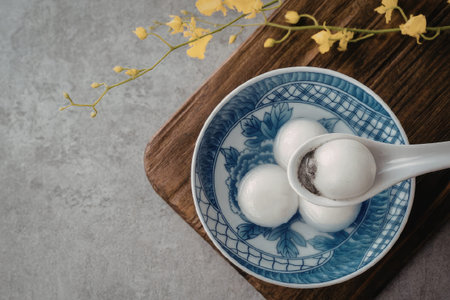 A blue bowl containing boiled eggs with a spoon, placed on a wooden board with yellow flowers in the background.の写真素材