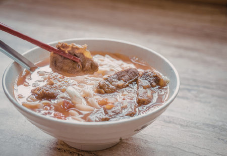 A steaming bowl of noodle soup with meatballs, garnished with vegetables and served with chopsticks.の写真素材