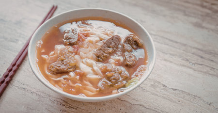 A steaming bowl of meatball soup with a rich tomato-based broth, served with chopsticks on the side.