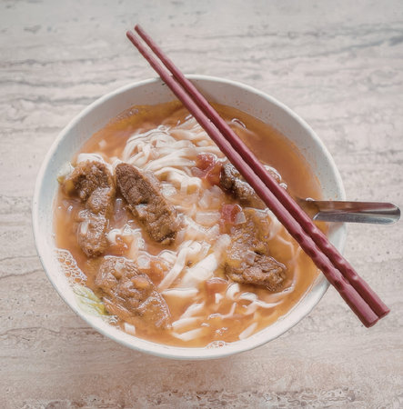 A steaming bowl of noodle soup with chunks of meat and vegetables, served with a pair of chopsticks...
