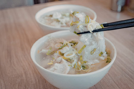A bowl of steaming hot chicken rice soup with green onions, served with chopsticks.