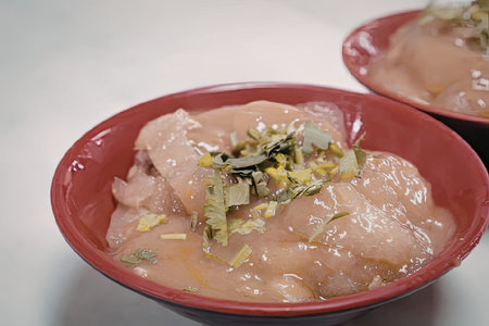 A close-up of a red bowl filled with a savory chicken dish, garnished with green herbs.