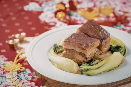 A plate of braised pork belly served with sliced vegetables on a decorative table setting.の写真素材