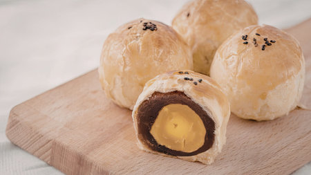 A close-up view of egg yolk pastry bites on a wooden cutting board, one cut open to reveal the gooey...