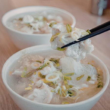 A bowl of steaming hot chicken and rice soup with green onions, served with chopsticks.
