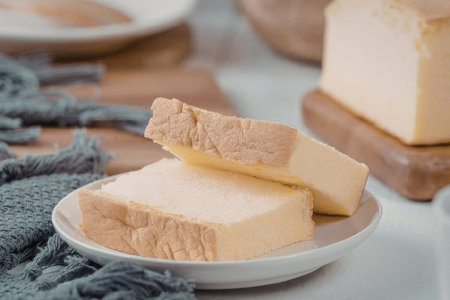 A close-up view of two slices of cheesecake on a white plate, with a blurred background featuring...