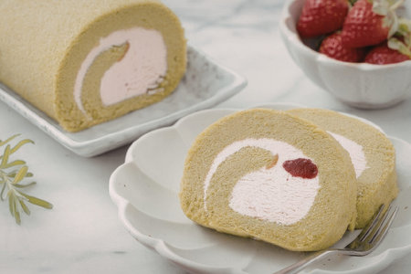 A green tea cake roll with pink filling and strawberries on the side
