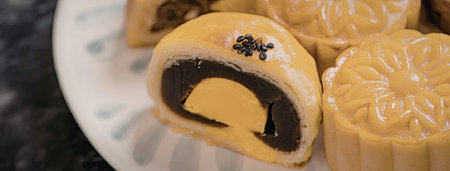 A plate of mooncakes, one cut open to reveal its dark filling, showcasing traditional design and...