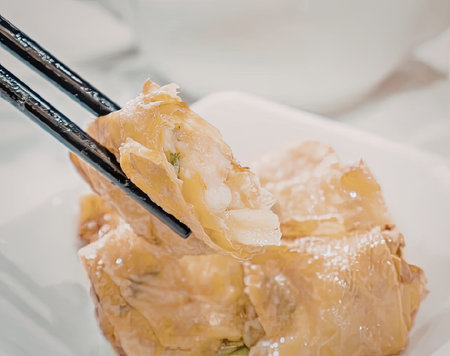 A close-up image of a crispy fried dumpling being picked up by chopsticks, served on a white plate.