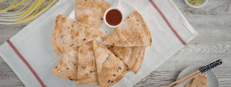 A plate of pan-fried dumplings served with a side of dipping sauce on a wooden table.