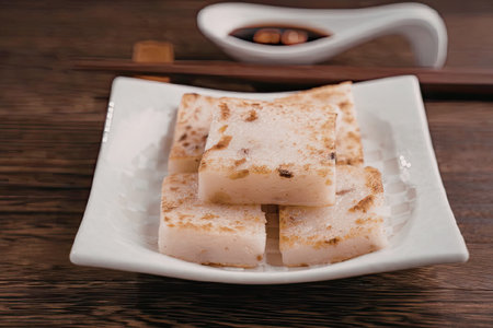 A plate of pan-fried dumplings served on a white square plate with a small bowl of dipping sauce in...